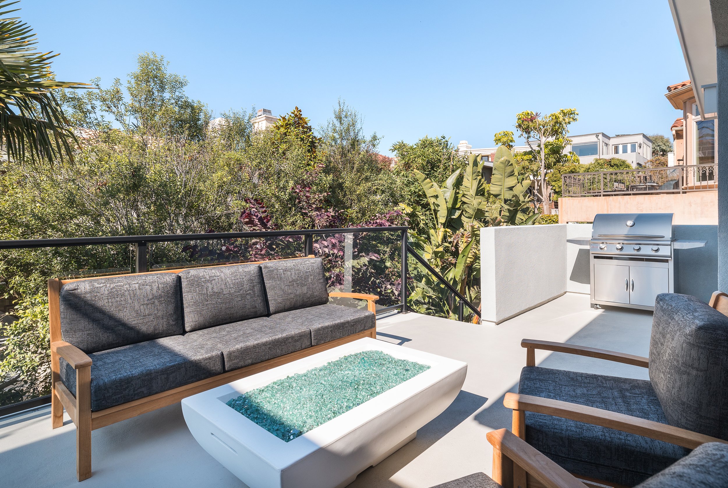 Remodeled balcony with grey sofas, white firepit and steel BBQ
