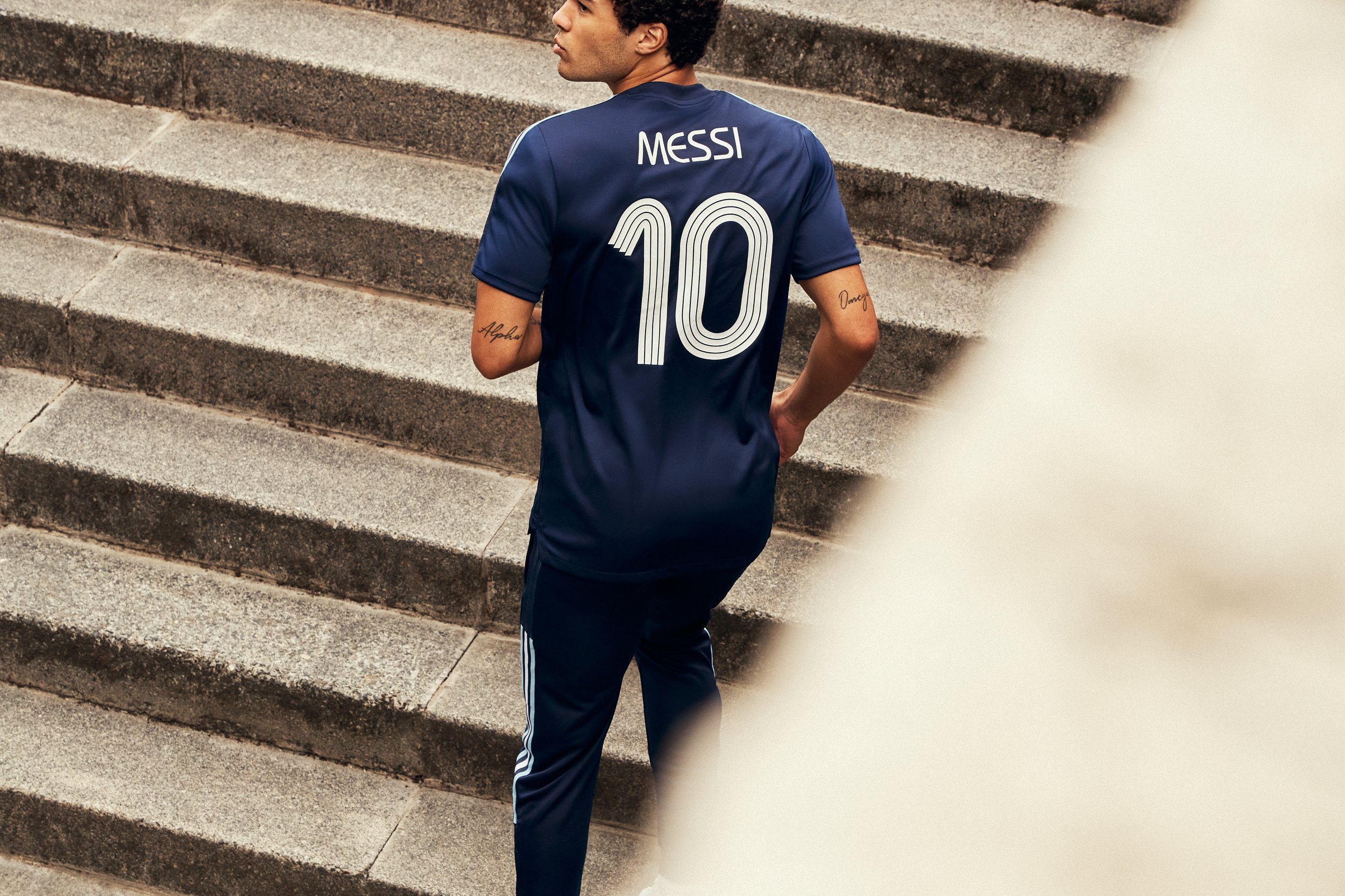 A man wearing a navy blue soccer jersey with the name 'Messi' and the number 10 on the back, walking up stone steps.