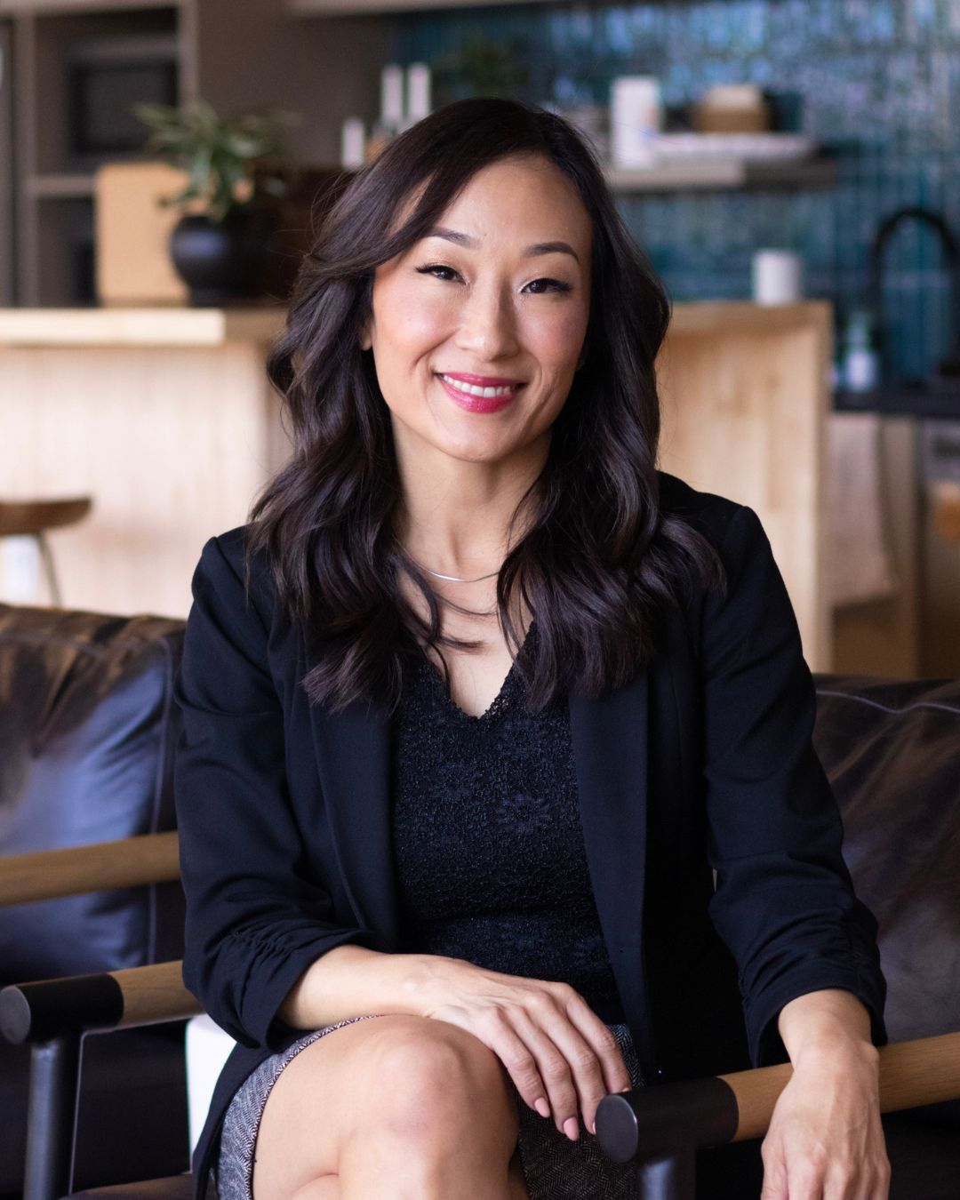 Professional portrait of Angela Jae Chun, a woman attorney, seated in an office setting, smiling and wearing a dark blazer.