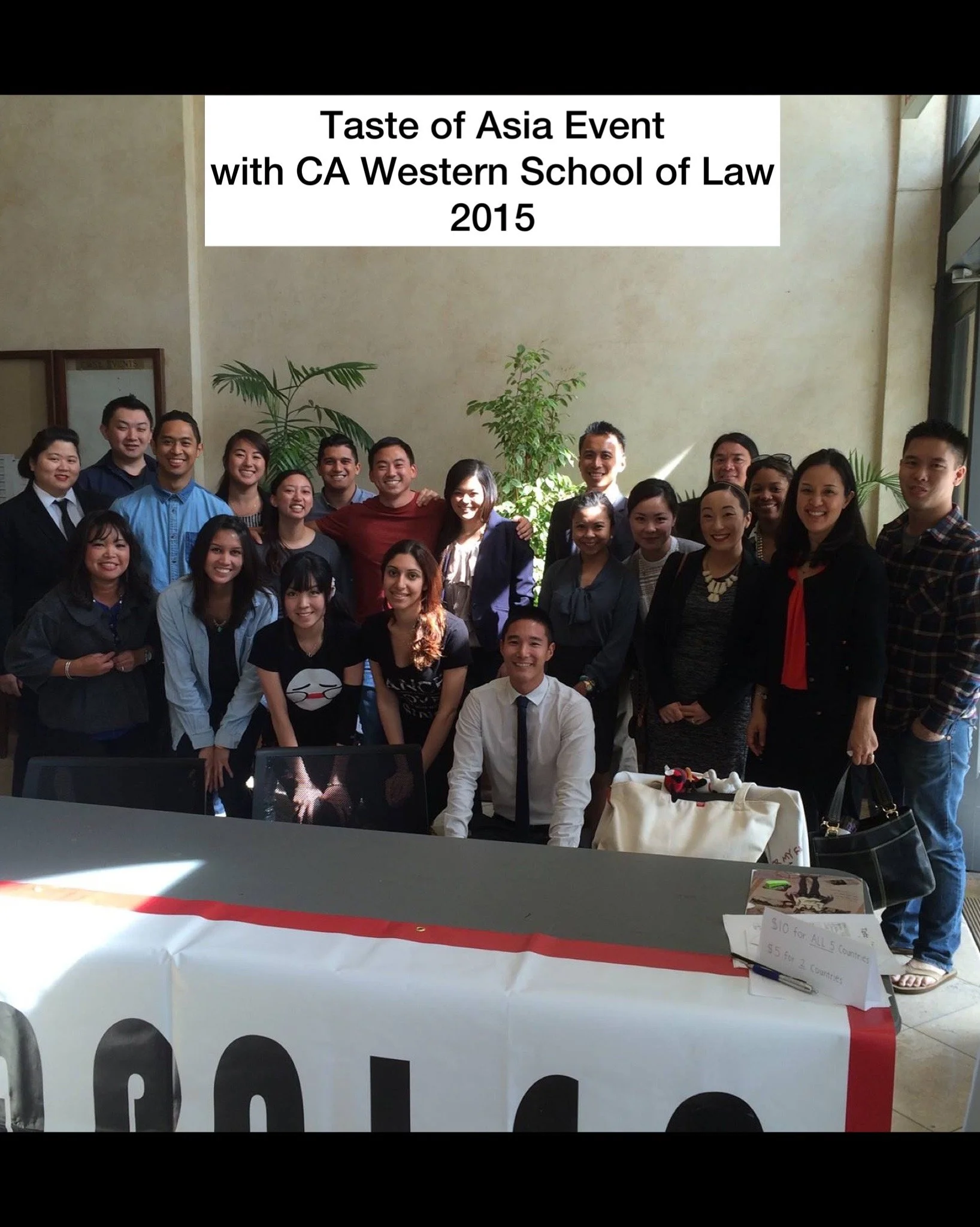 Group of people attending the Taste of Asia event with CA Western School of Law in 2015, gathered indoors with plants and sunlight in the background.