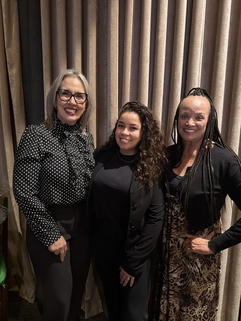 Three women dressed in business casual attire pose for a photo.