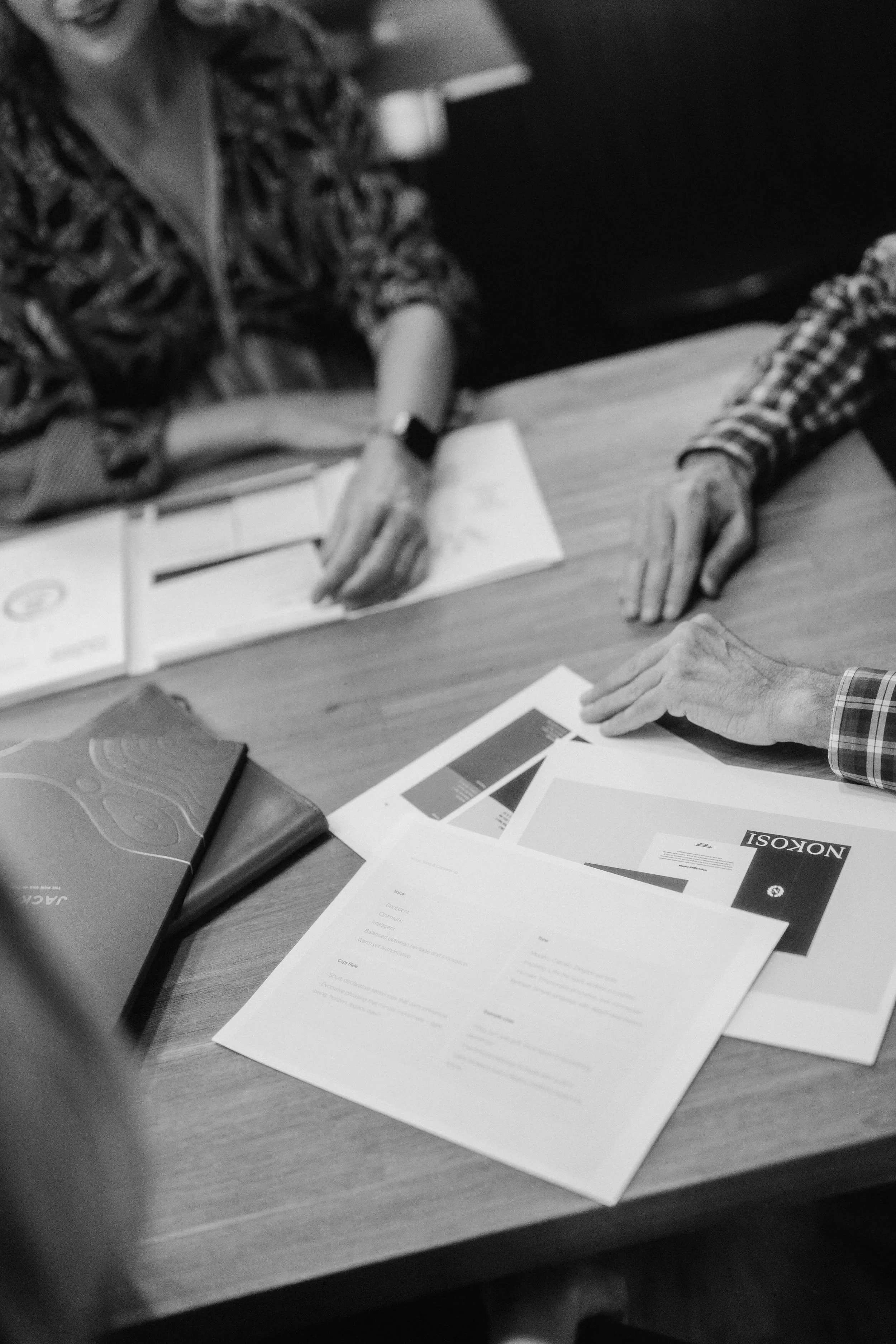 People sitting at a table with papers, brochures, and folders, possibly in a meeting or discussion.