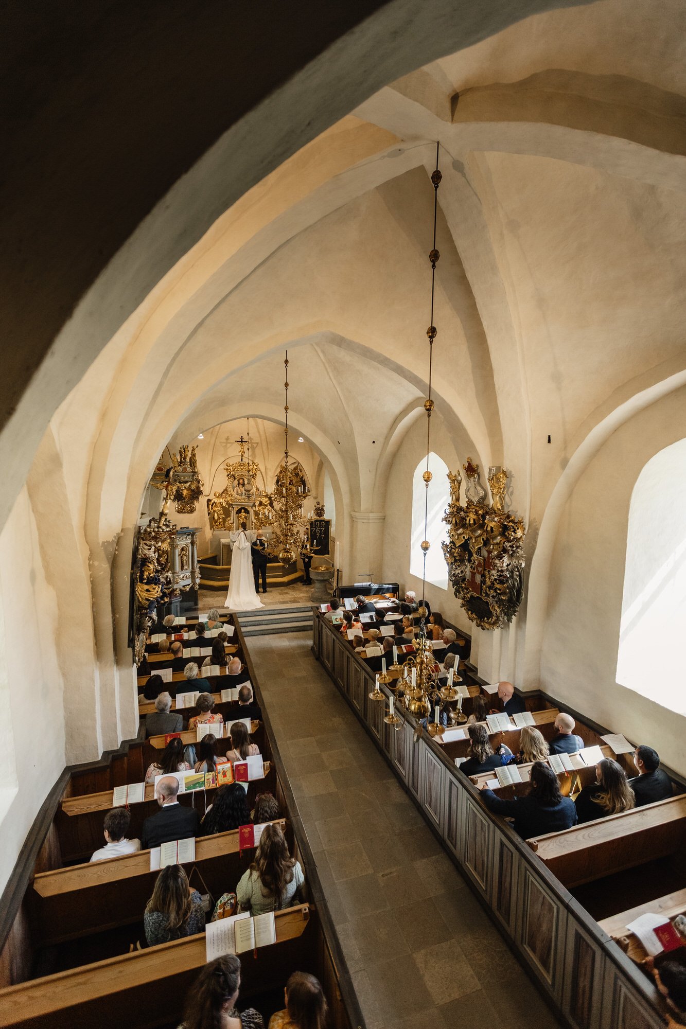 Interiör av en Låssa under en gudstjänst med folk som sjunger och läser ur böcker, altar med kors och religiösa dekorationer i bakgrunden.