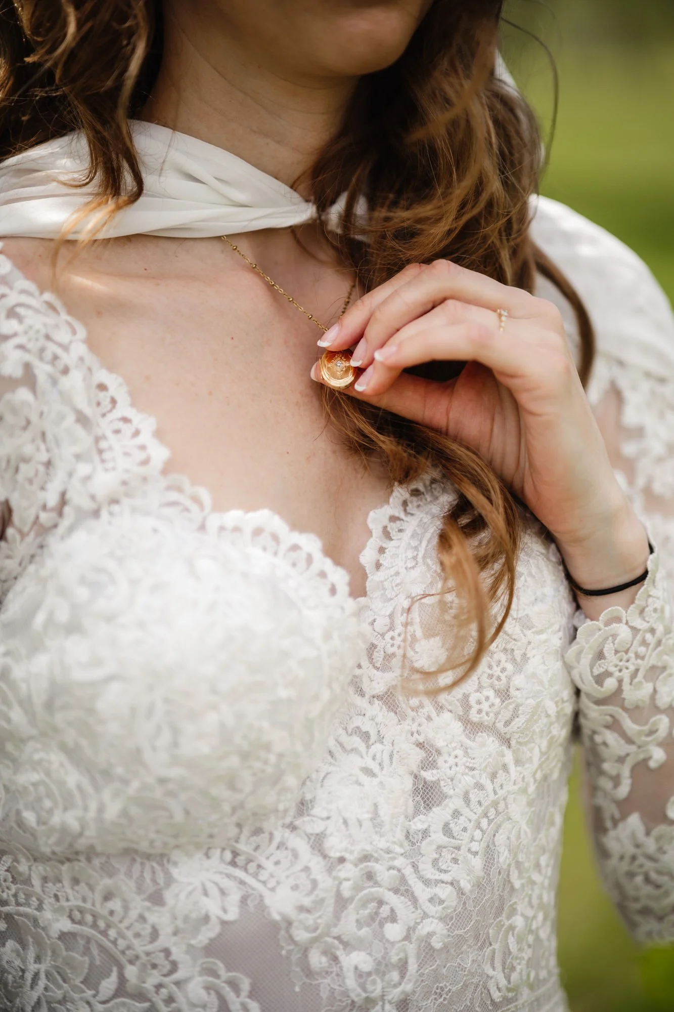 Detalj av en kvinna i vitt spetsbröllopsklänning, med halsband och ring, håller i ett halsband.
