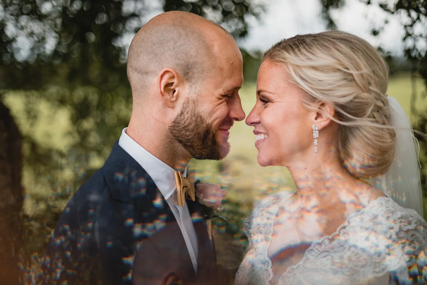 Brudpar ler mot varandra i ett nära och naturligt bröllopsporträtt utomhus fotograferat i mjukt ljus.