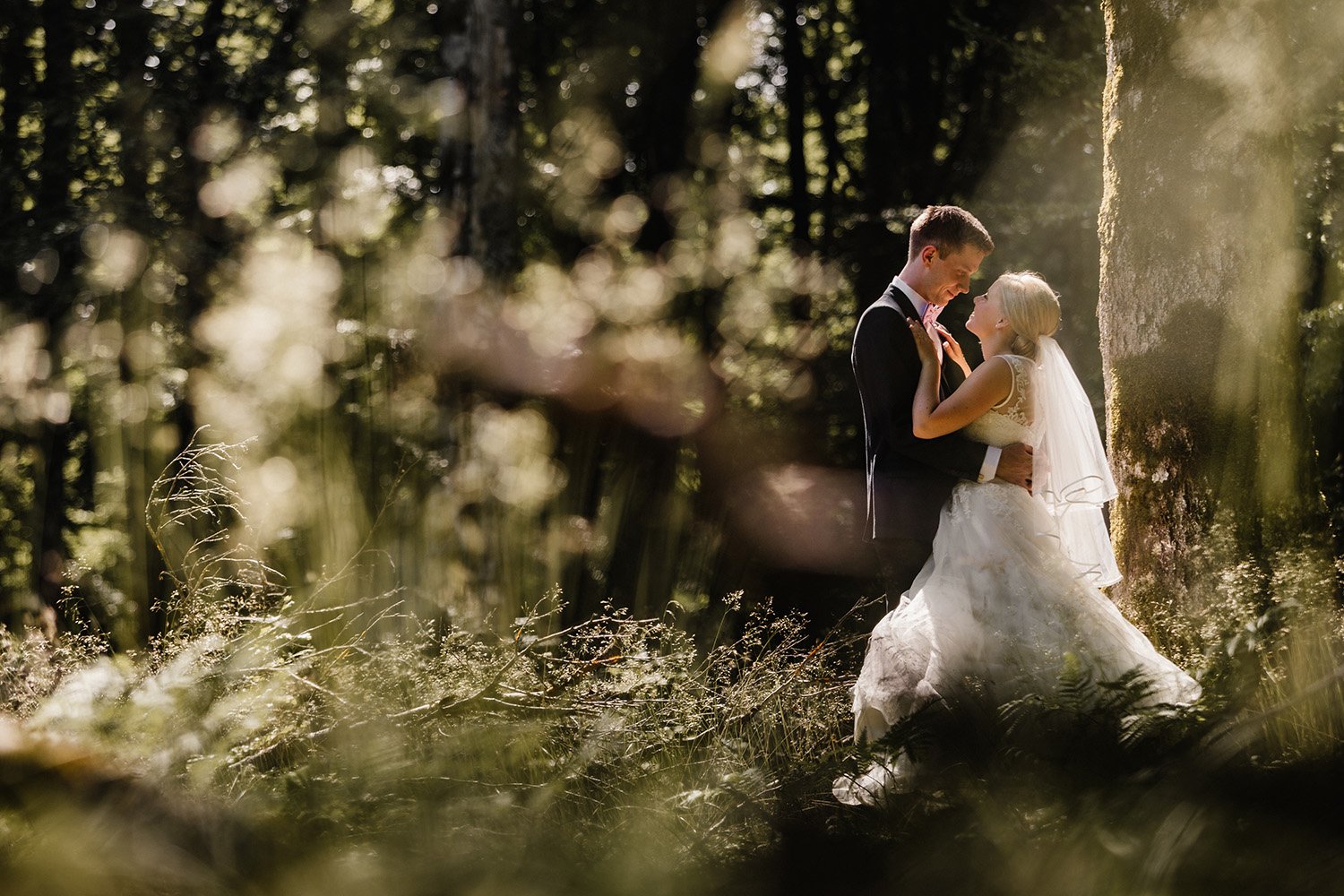 Brudpar står tillsammans i skogsmiljö under ett drömskt och romantiskt bröllopsporträtt med naturligt ljus.