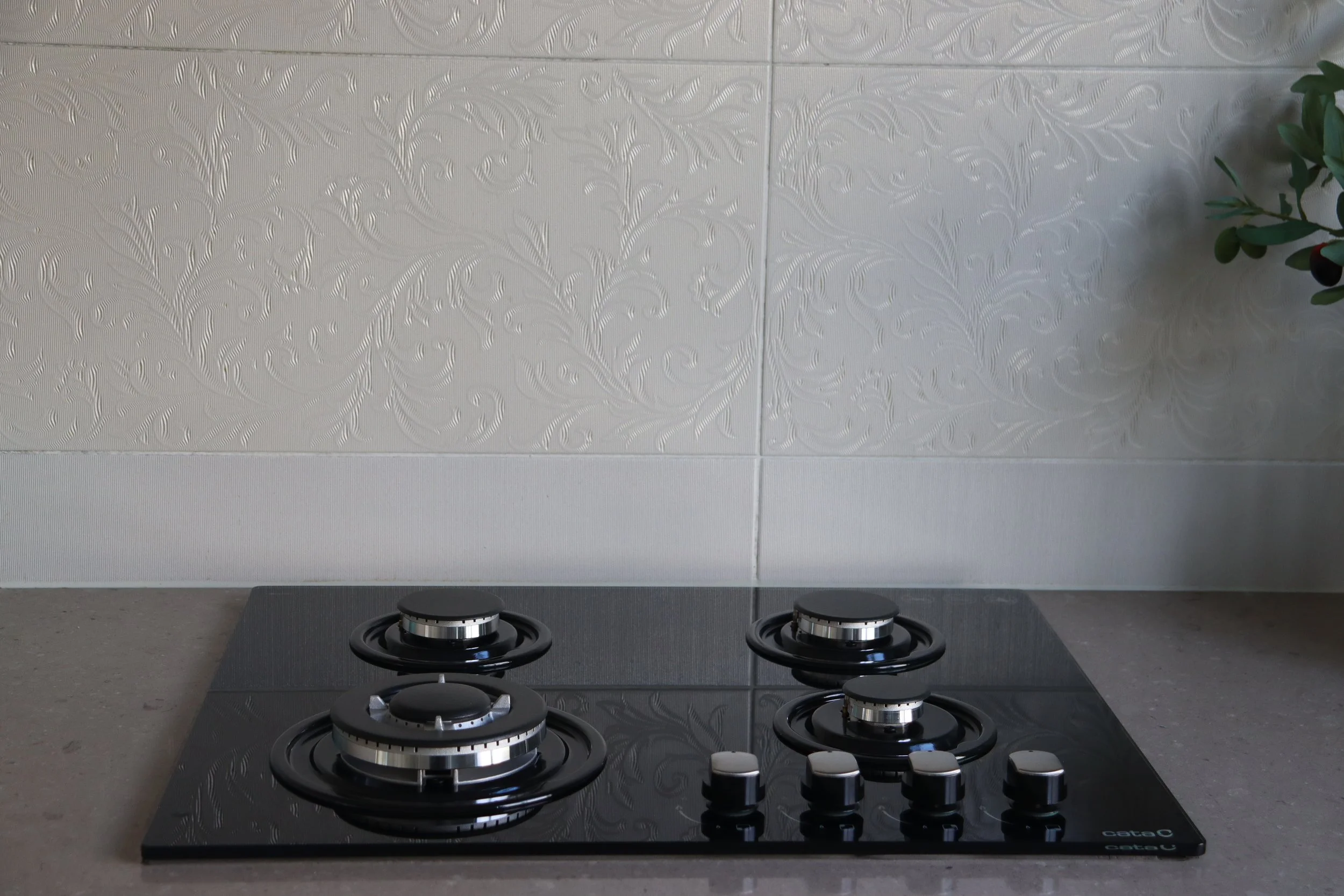A black gas stovetop with four burners on a light gray countertop in front of a textured wall.