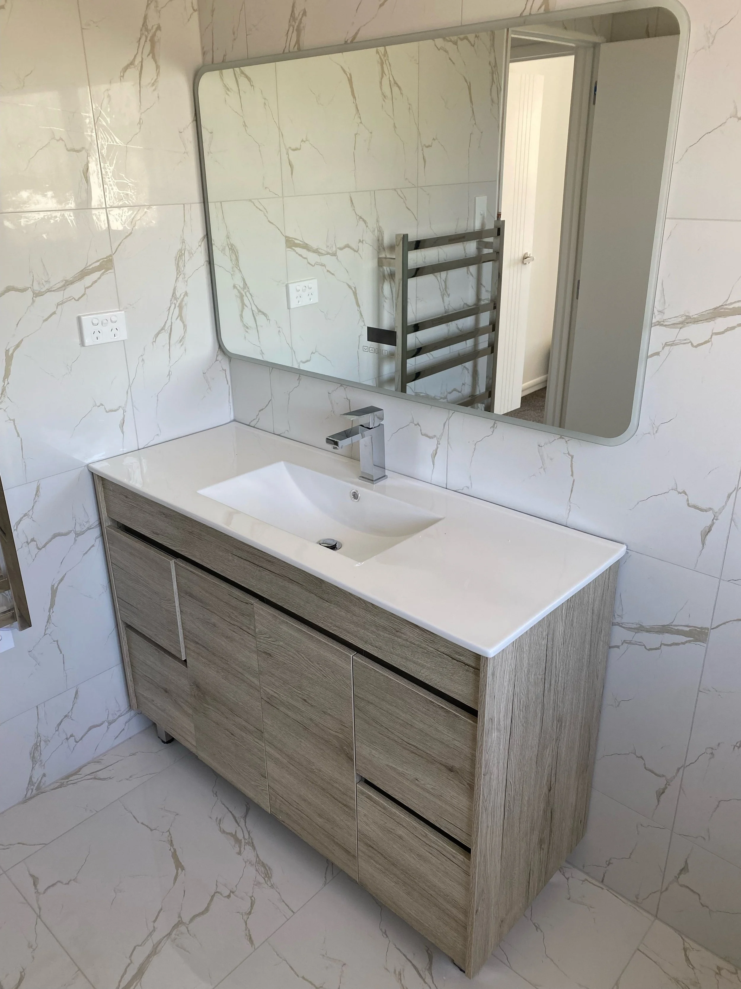Bathroom sink with a wooden cabinet, large rectangular mirror, and marble wall tiles.
