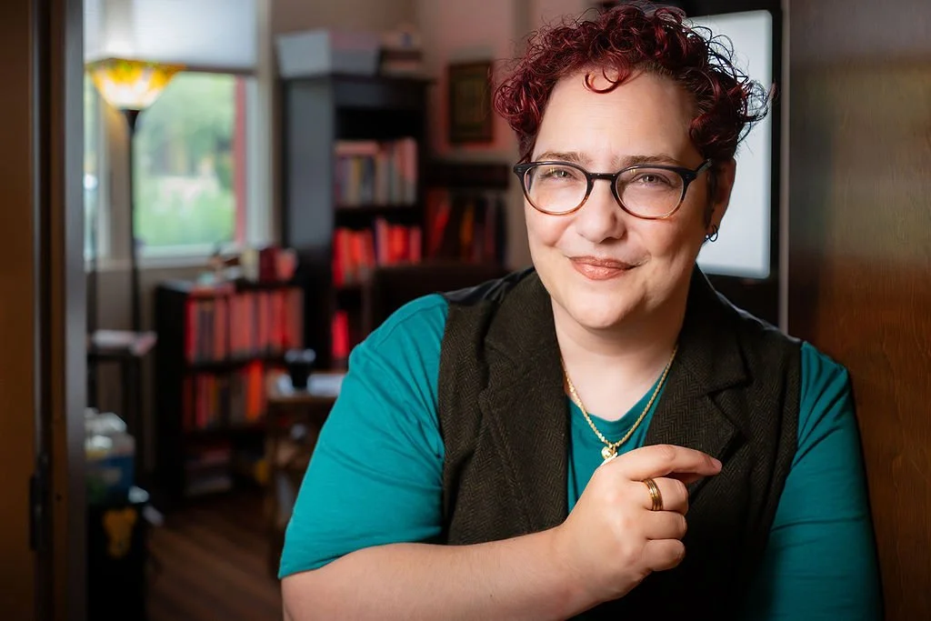Non-binary person with purple hair, and a teal shirt standing in a doorway.
