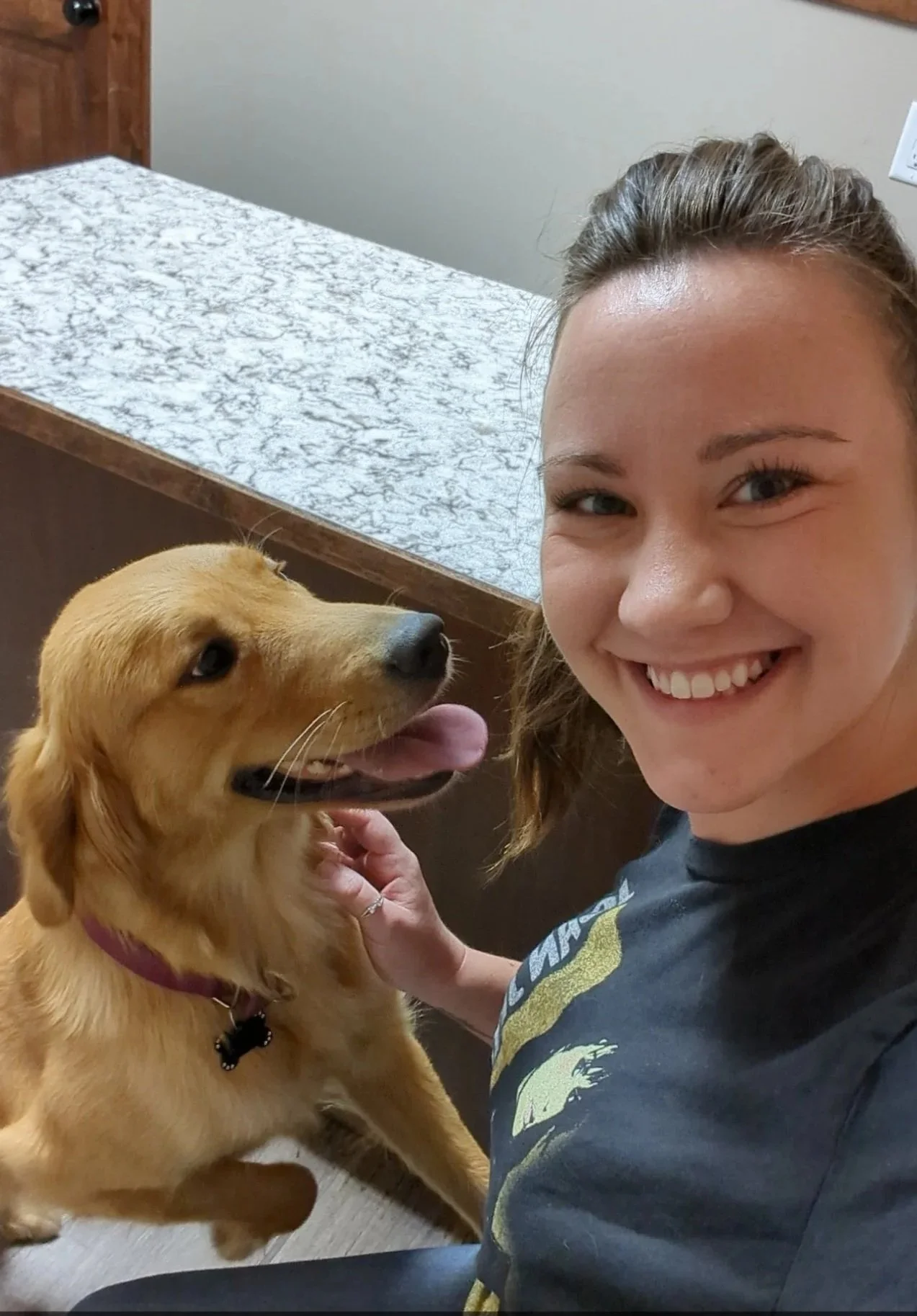 A woman smiling and looking at the camera with a golden retriever dog that appears happy, looking up at her with its tongue out.