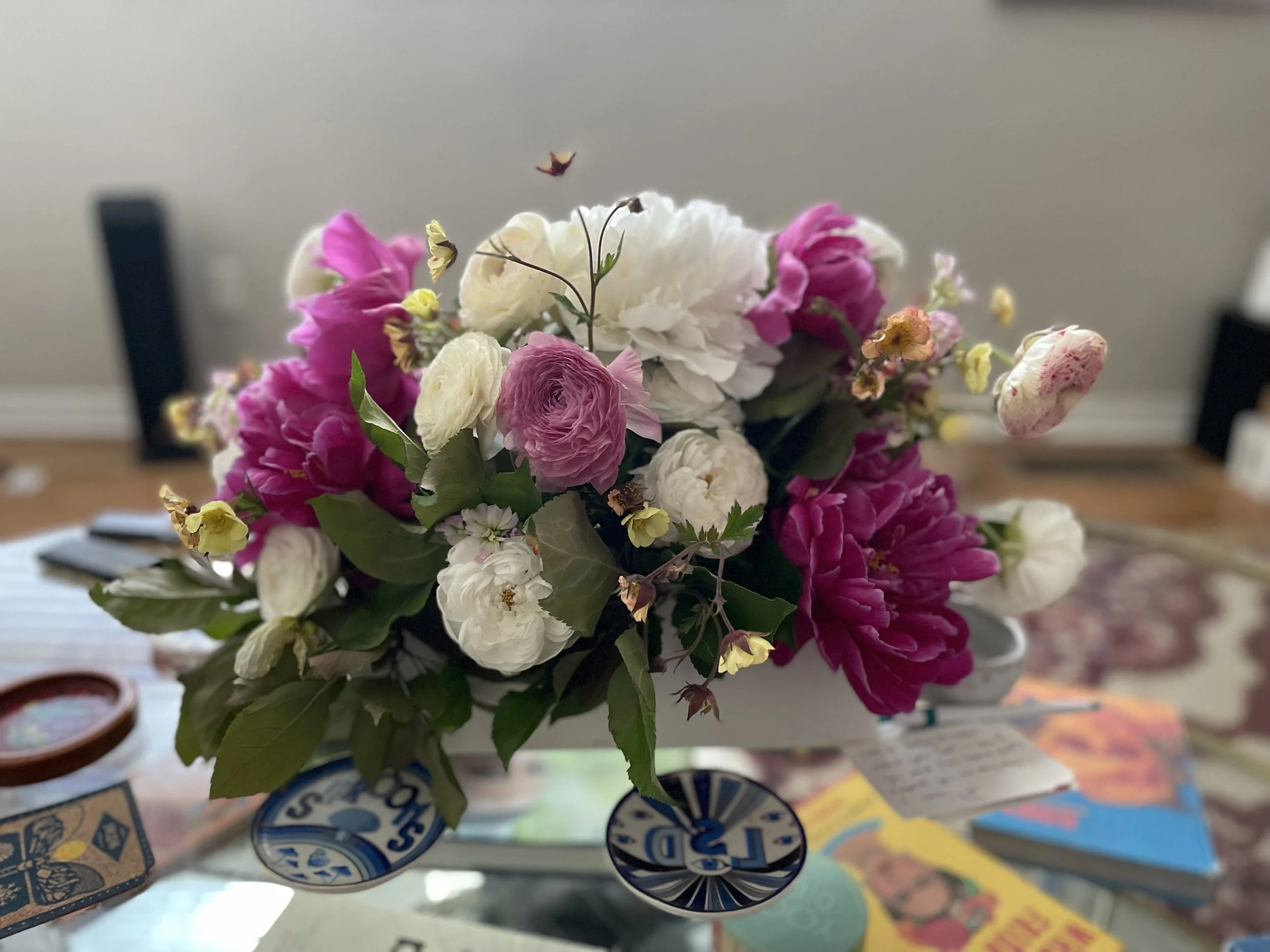 A colorful bouquet of pink, white, and cream flowers on a table with various objects and cards.