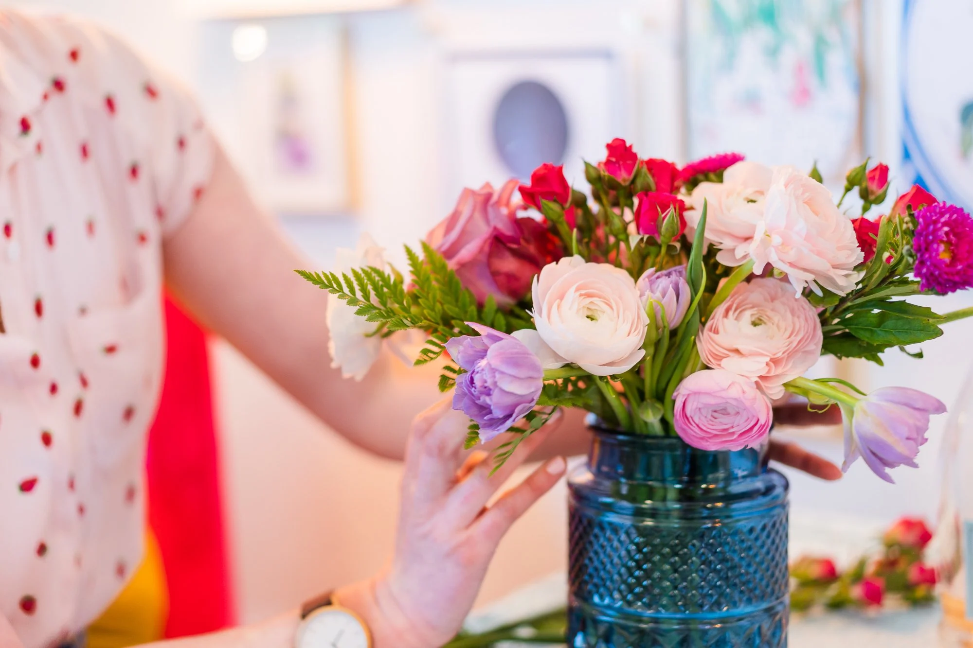 Person arranging a colorful bouquet of flowers in a dark blue vase.