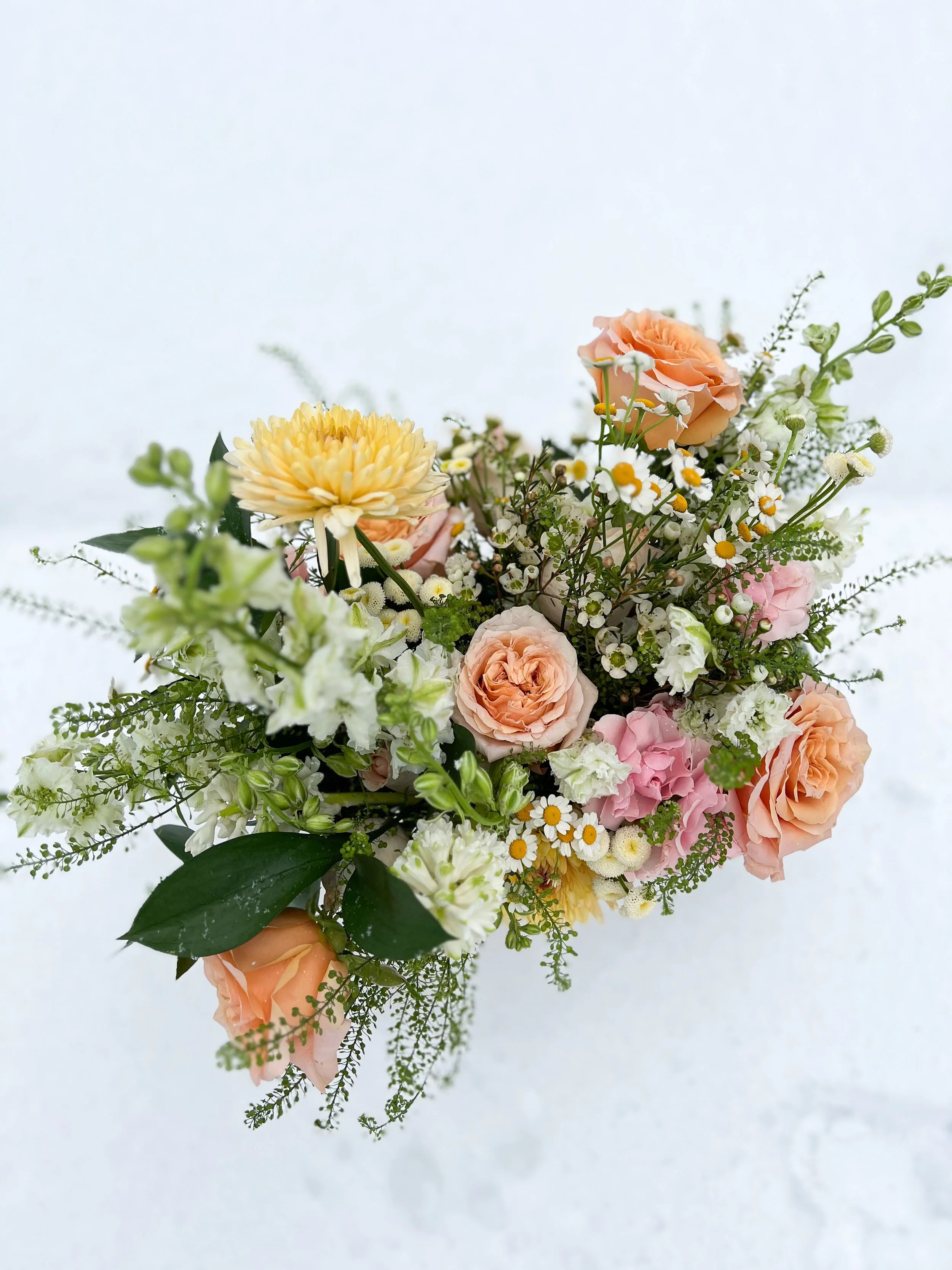 A bouquet of pastel-colored flowers including roses, daisies, and other small blossoms against a white background.