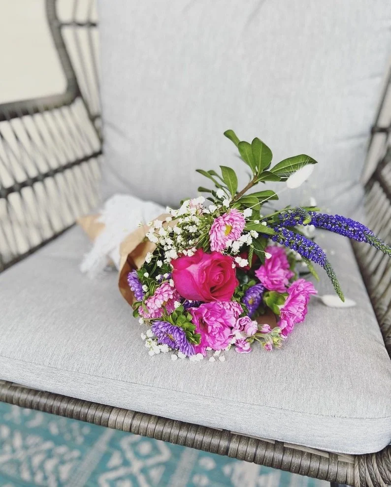 A bouquet of pink, purple, white, and green flowers resting on a gray cushioned chair.
