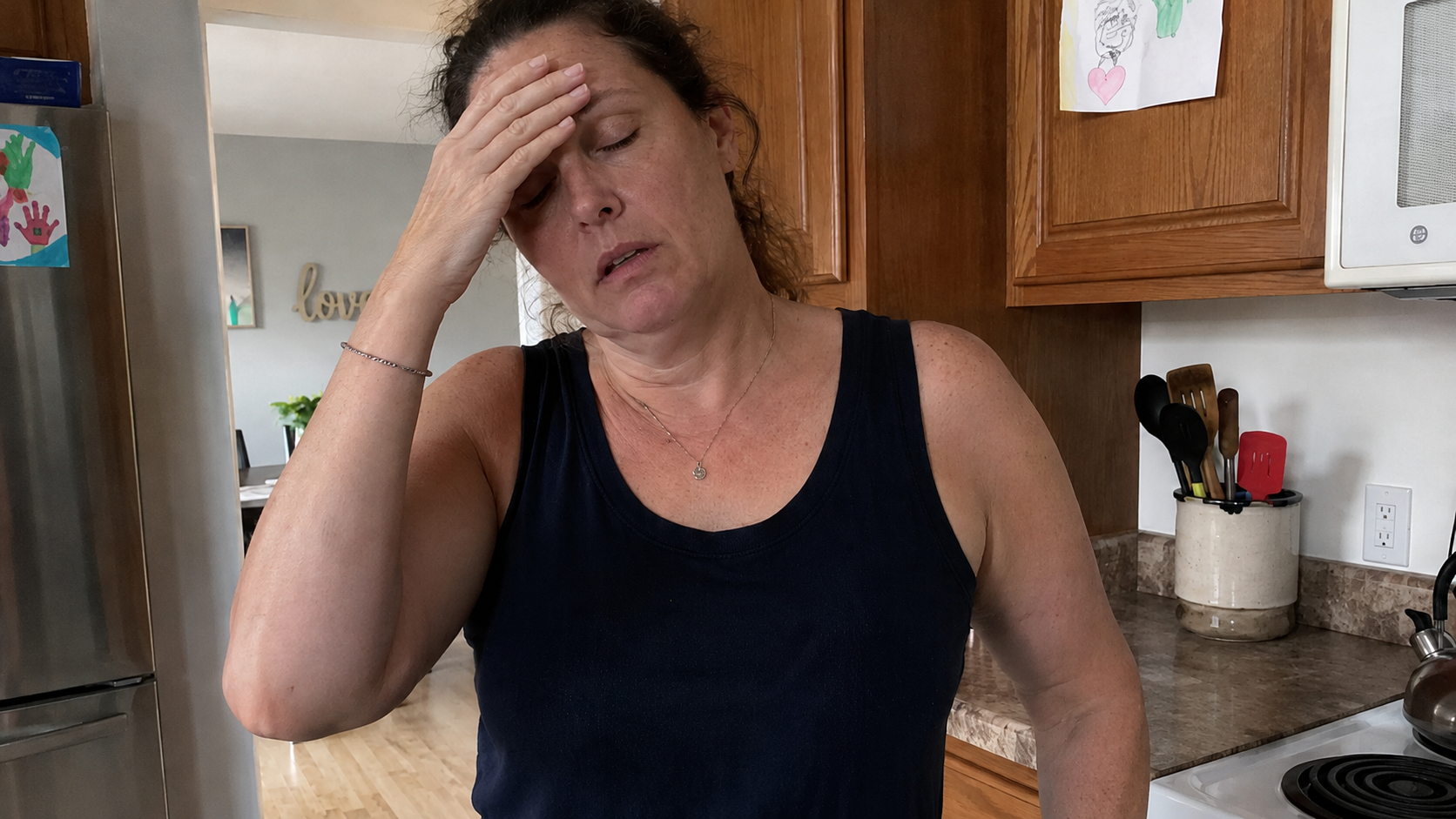 "Woman pressing hand to forehead in her kitchen — brain fog and forgetfulness in midlife during perimenopause and burnout"