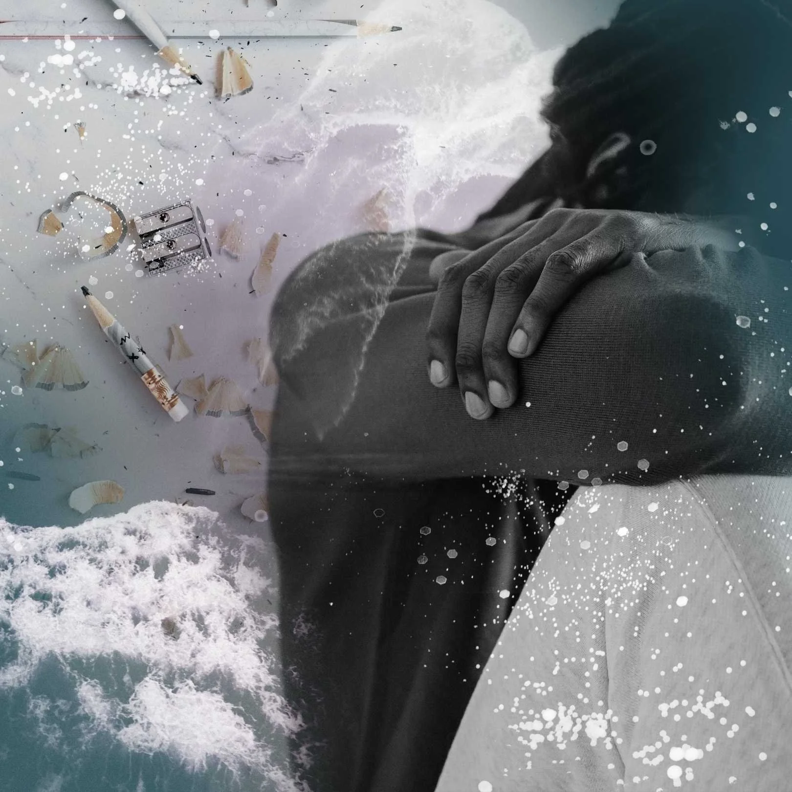 A person with their head in their hands before scattered pencils and shavings with ocean waves