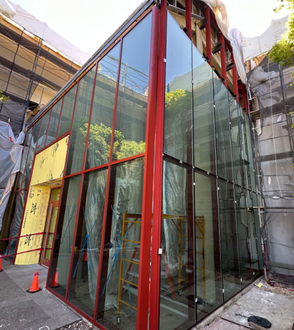 Construction site with a modern glass building featuring red framing, scaffolding, and construction materials.