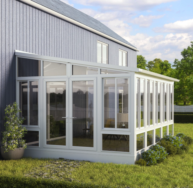 A sunroom with glass walls and white framing attached to a blue house, surrounded by a grassy yard with plants and trees.