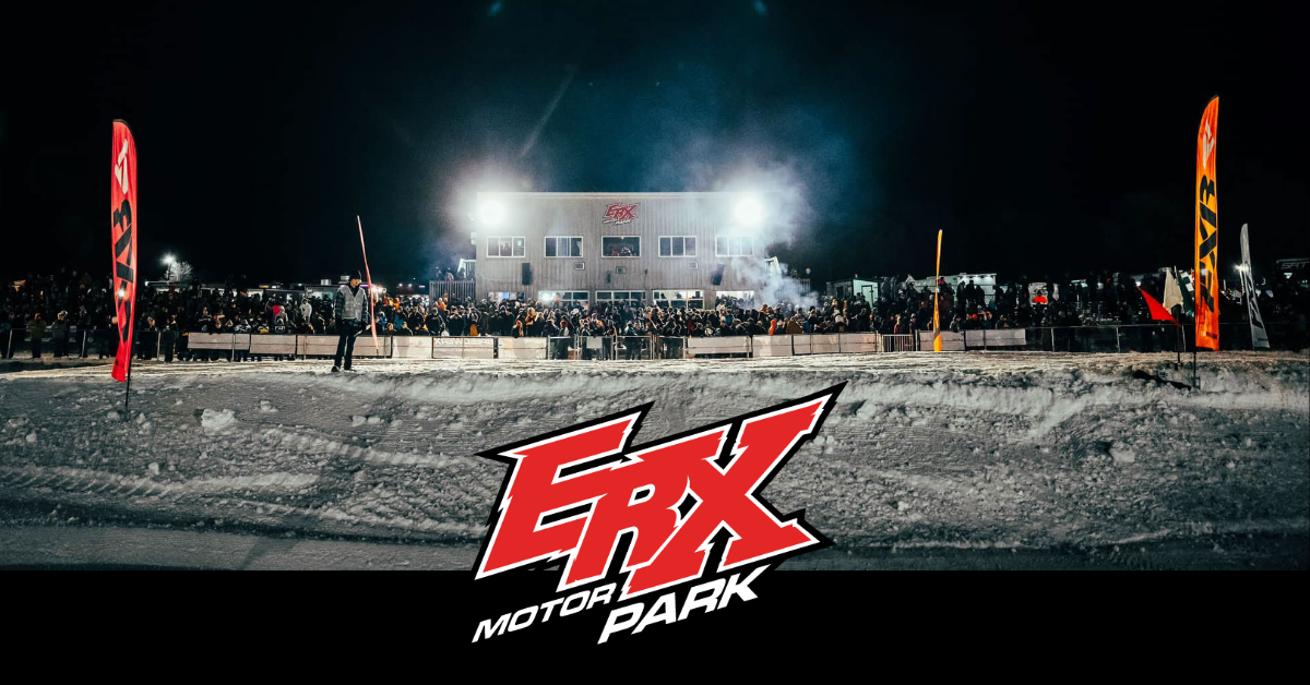 Night scene at ERX Motor Park with a large crowd gathered, illuminated by bright lights, and flags on either side displaying ERX branding on a snowy ground.