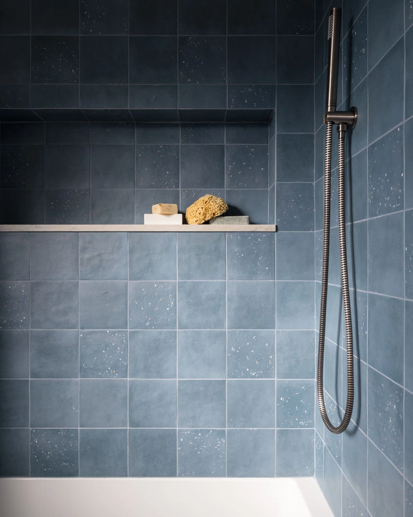 This shower design brings blue tile to life by mixing solid finishes with subtle speckled detailing; creating depth, movement, and just the right amount of visual intrigue. The contrast is soft but intentional, proving that even within a single color