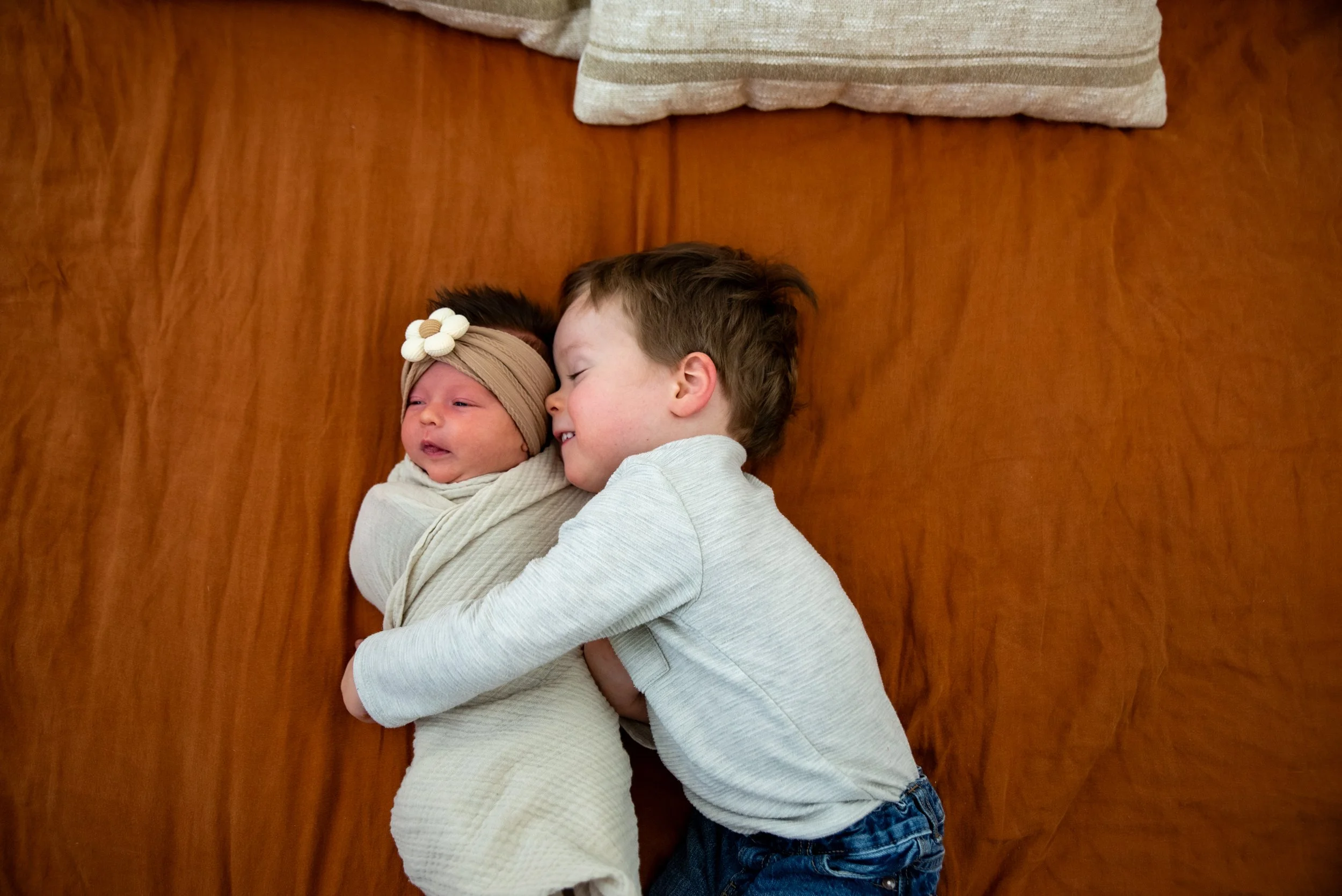 A young boy is hugging a newborn baby girl on a wooden surface.