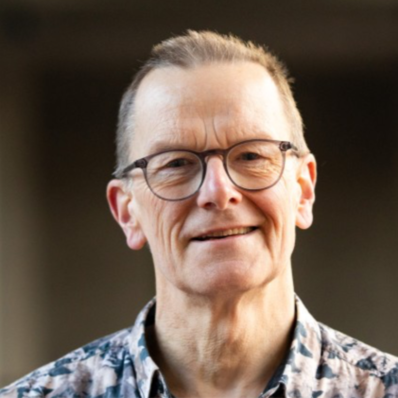 A middle-aged man with glasses smiling outdoors.