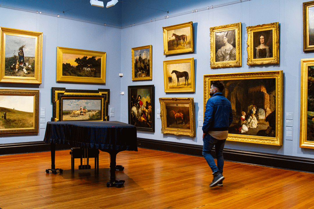 Man walking in room with walls covered in paintings.