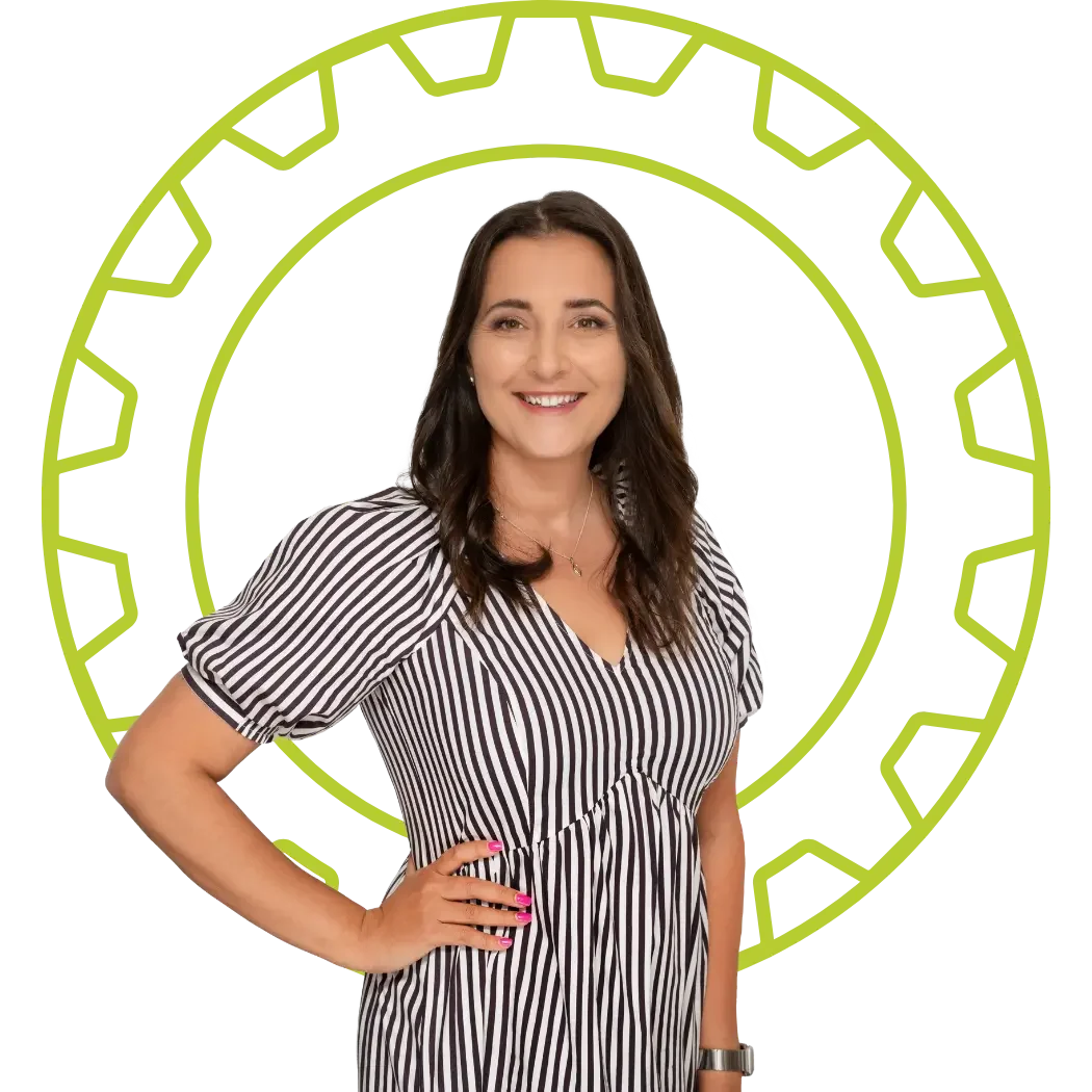 A woman with dark brown hair wearing a black and white striped dress, smiling with her hand on her hip in front of a lime green cog like shape.