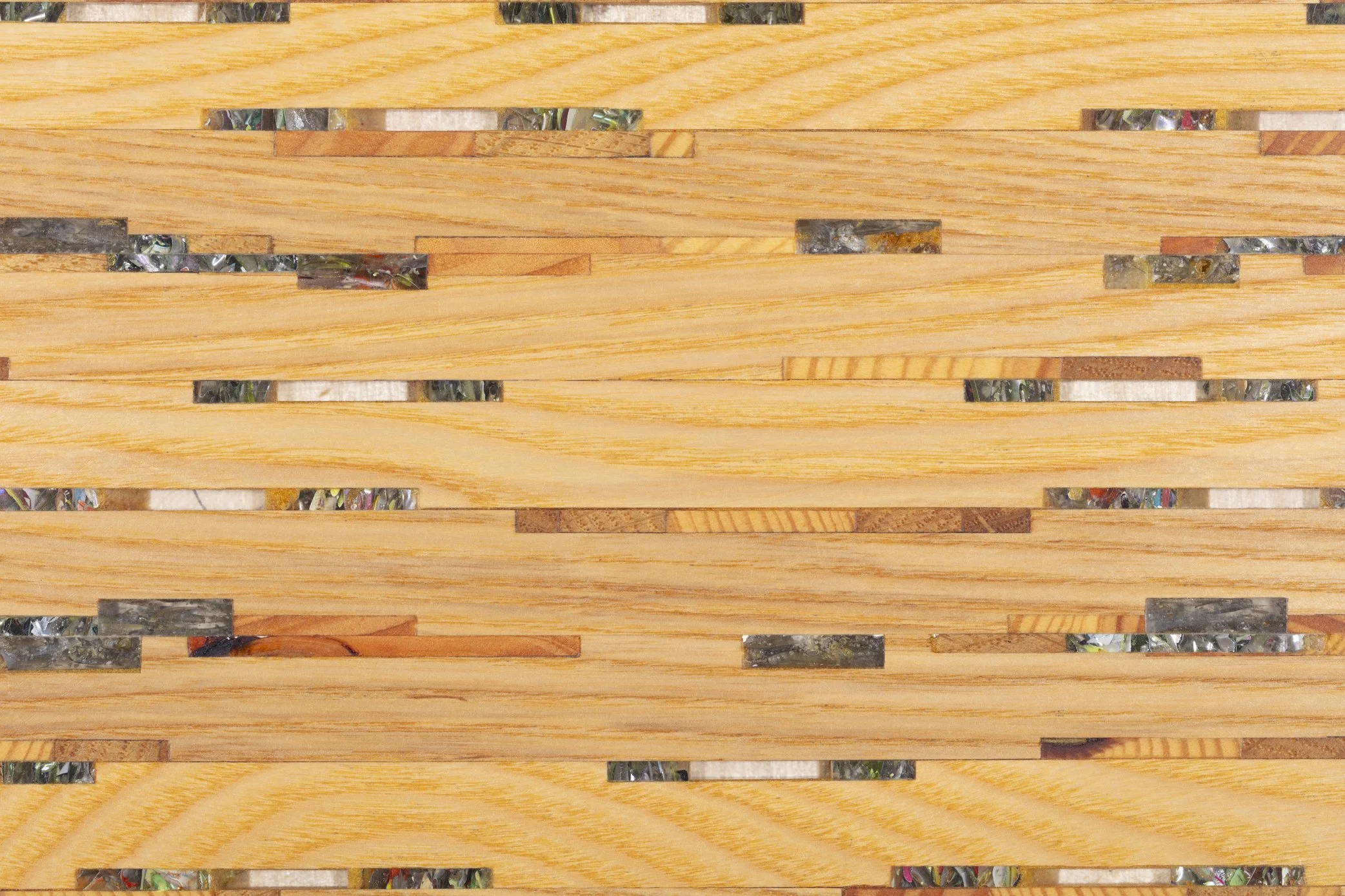 Close-up view of a wooden slatted surface with small gaps, revealing a shiny, colorful mosaic underneath.