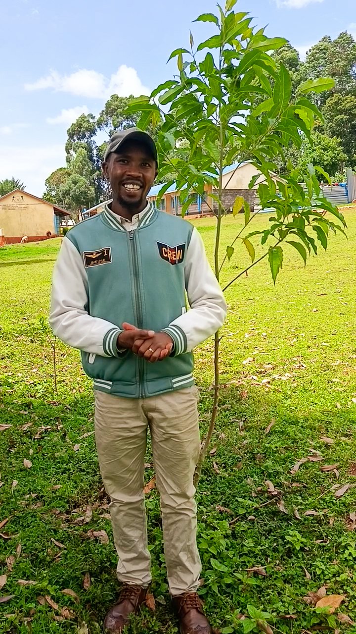 Billy Kiptoch stands proudly in front a young tree he planted