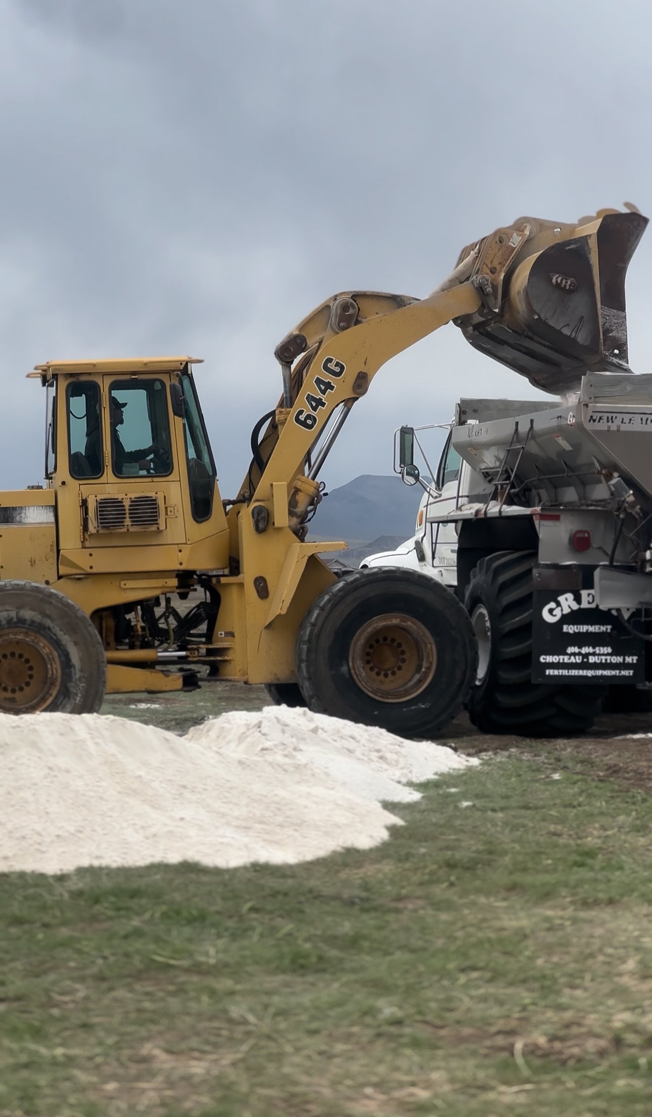 spreading natural fertilizer to help amend the soil. He is spreading gypsum. He is loading gypsum into the spreader box.