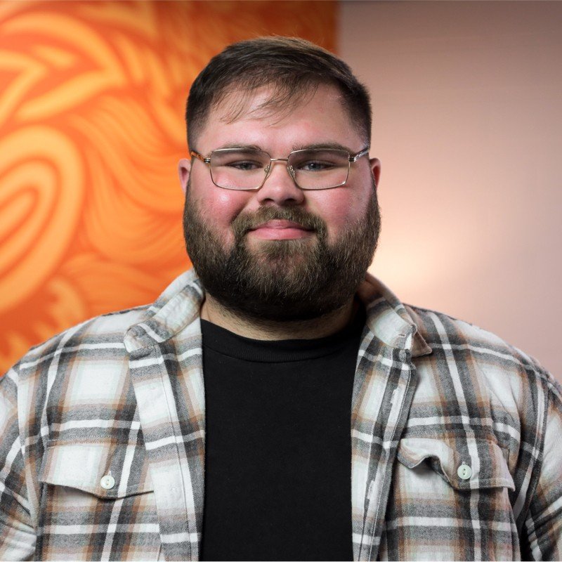 Man wearing glasses and a plaid shirt with an orange patterned background.