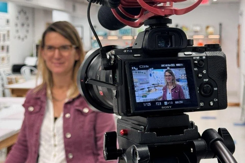 The owner of Glassworks Studio is being filmed or photographed with a camera in an indoor setting.