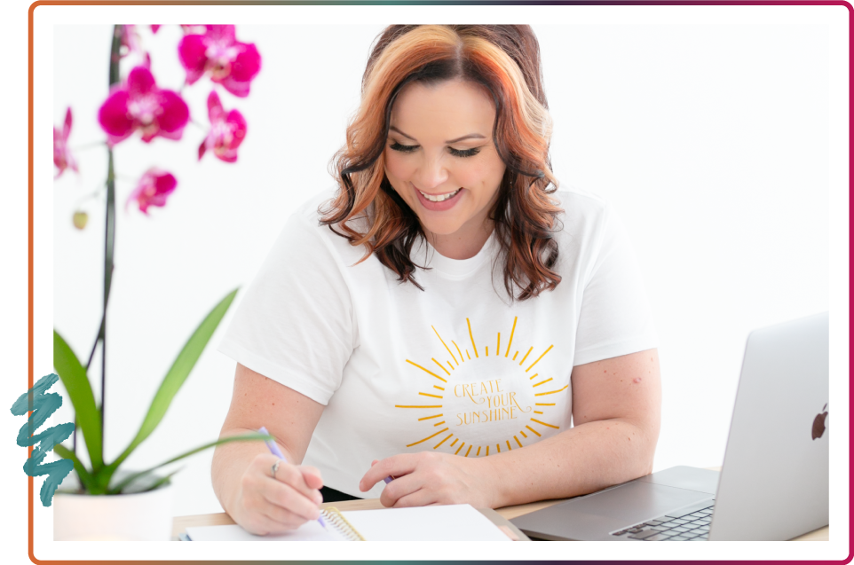Stephanie smiling and writing in a notebook with her laptop next to her