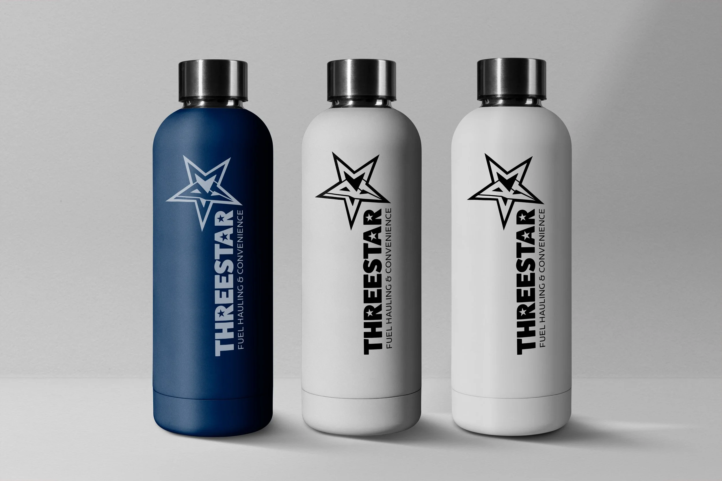 Three cylindrical bottles with metallic caps featuring a star and mountain logo, labeled "THREESTAR FUEL HAULING & CONVENIENCE," in blue, white, and black, standing in front of a plain gray background.