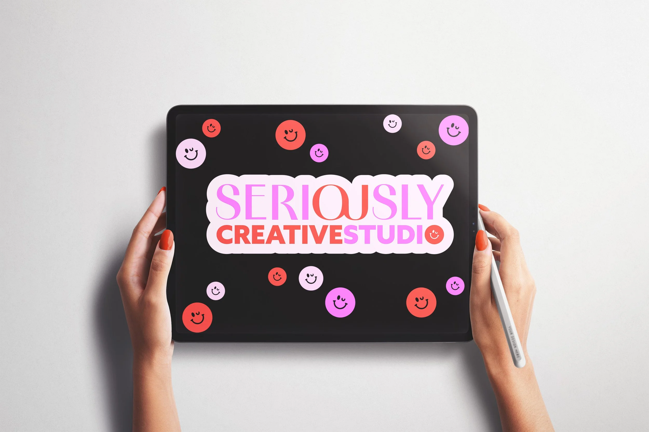 Person holding a stylus and tablet displaying colorful smiling face icons and text that reads "SERIOUSLY CREATIVE STUDIO" in pink, purple, and red font.