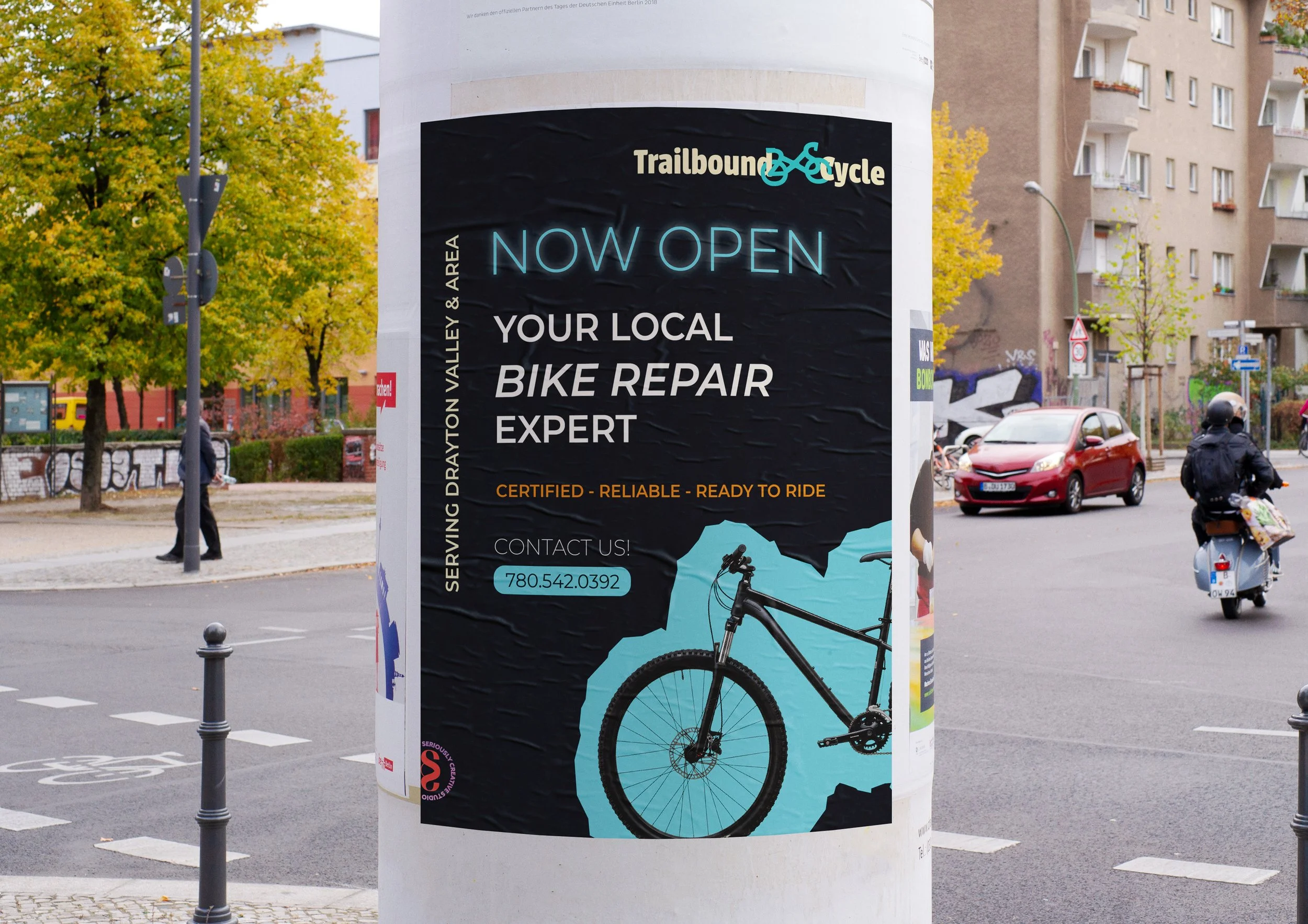 A city street scene with a large poster on a round white column advertising a bike repair business, with the words 'Now Open' and 'Your Local Bike Repair Expert.' The poster features a silhouette of a mountain bike and contact information, surrounded