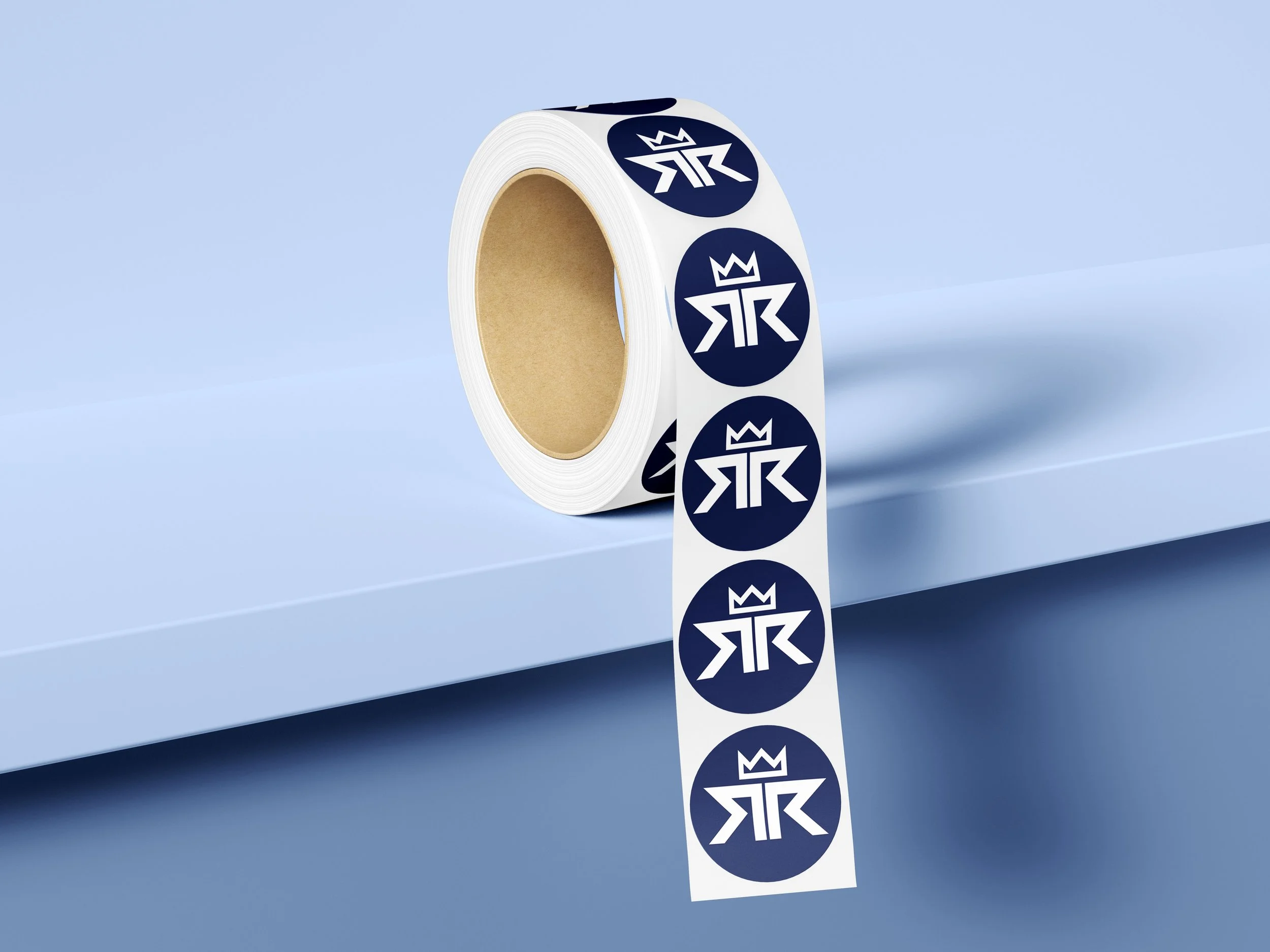 A roll of white sticker tape with navy blue circular stickers featuring a stylized crown and letter logo, placed on a light blue surface.