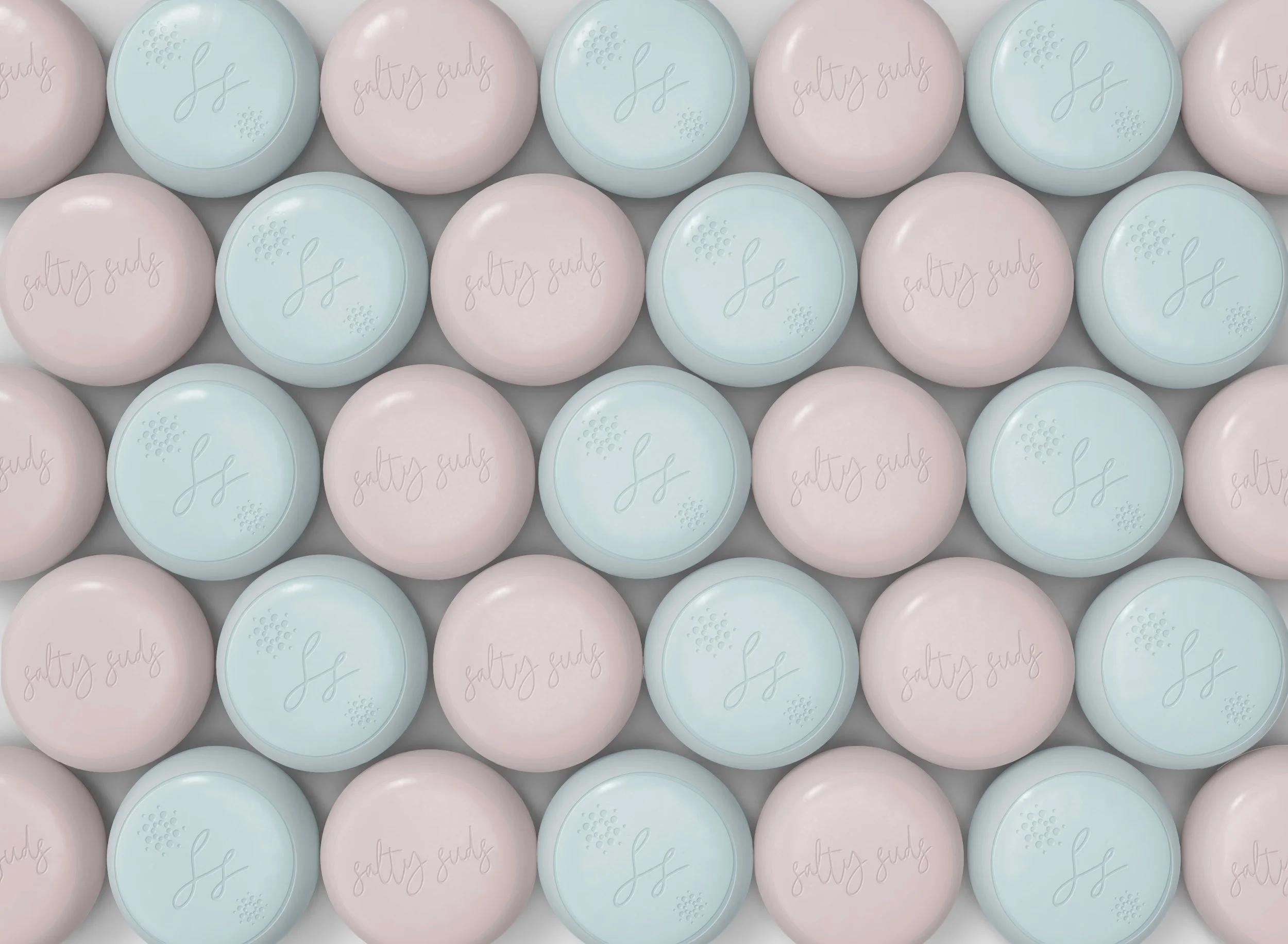 A pattern of round soap bars in pastel colors of pink and light blue, each embossed with the words 'salty sage' in cursive and a small decorative design.
