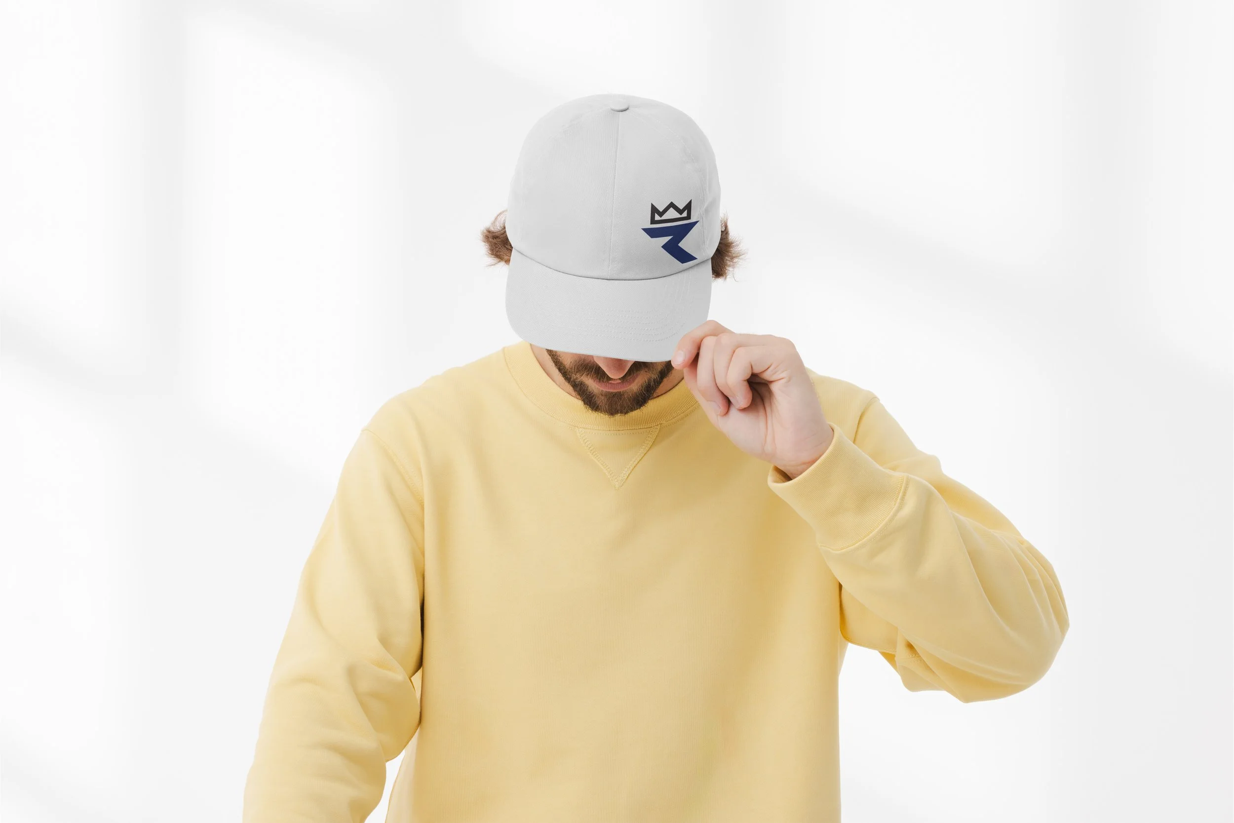 Person wearing a white cap with a black and blue logo, covering their face, and dressed in a yellow sweatshirt against a plain white background.
