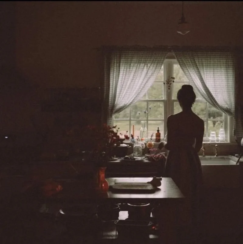 Woman pausing alone in a dim kitchen, showing why someone might turn toward body-based work
