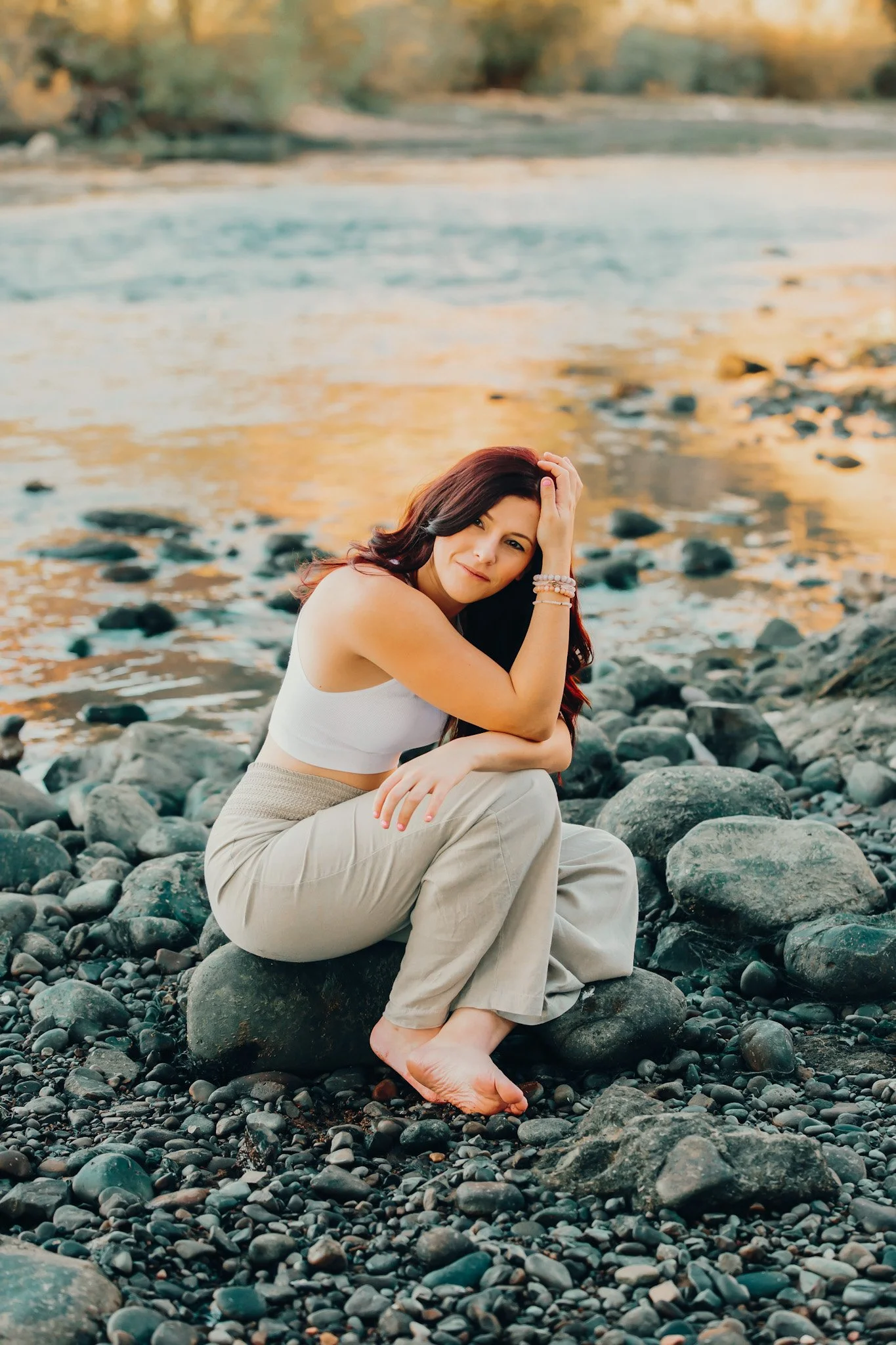 A woman sitting on rocks by a river, with her feet on the rocks, during sunset.