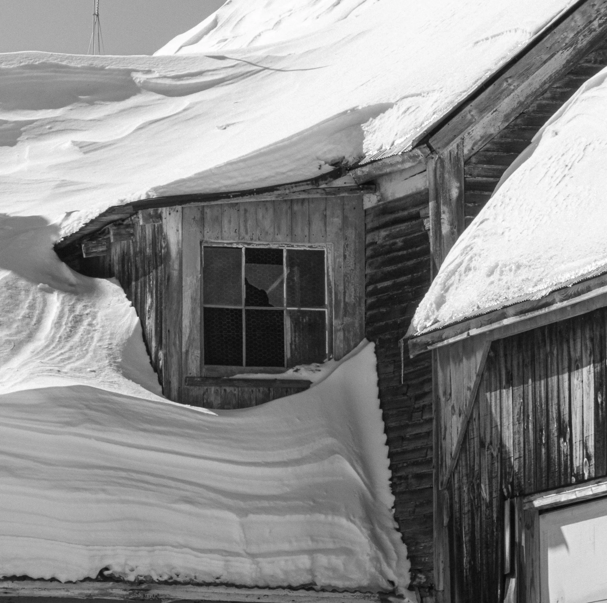 Layers of snow stack up in the corners of the roof overlooked by the window. 