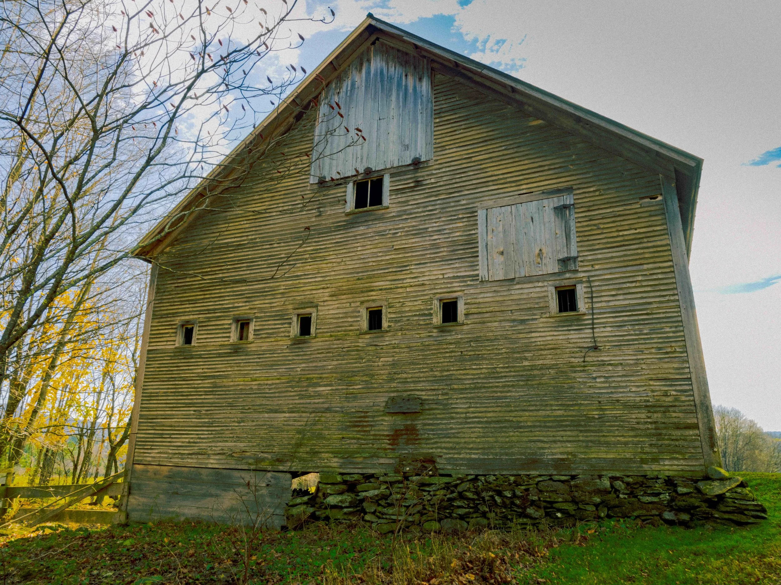 A yellow Vermont barn during the autumn. The well worn wood losing a bit of its color.