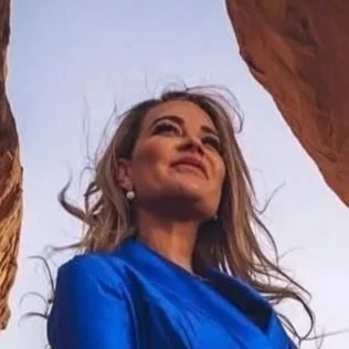 A woman in a vivid blue dress standing in a rocky canyon with sunlight illuminating the rock formations.