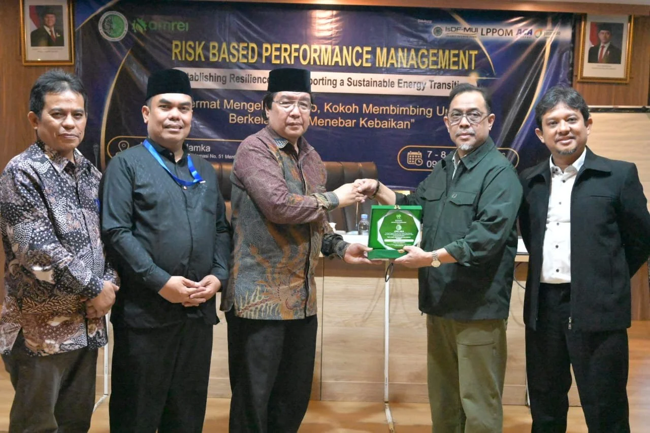 Six men standing in a row at a conference, with two men in the center exchanging a green award plaque. A banner behind them reads 'RISK BASED PERFORMANCE MANAGEMENT' and mentions a conference about resilient and sustainable energy transition. There are framed photographs of officials on the wall behind them.