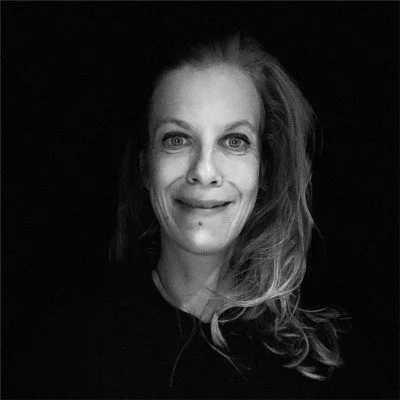 Black and white portrait of a smiling person with long hair against a dark background.