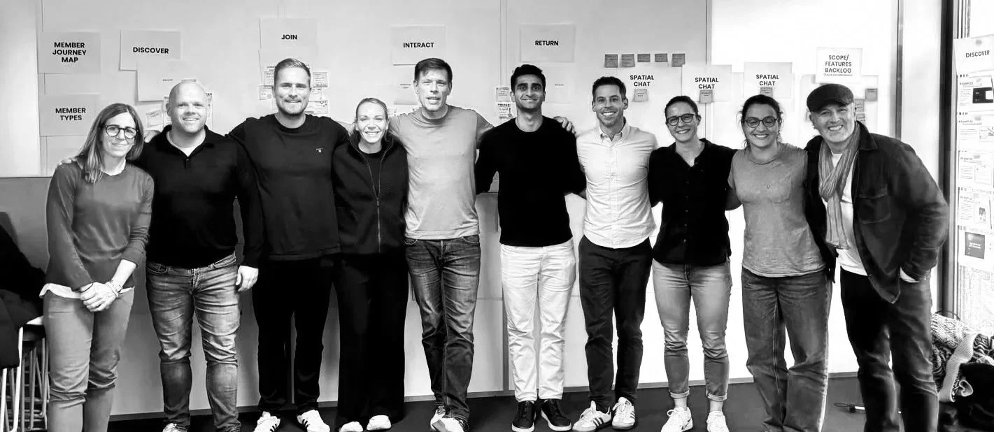 Group of ten people standing in a row indoors with a wall of charts and notes behind them, smiling at the camera.