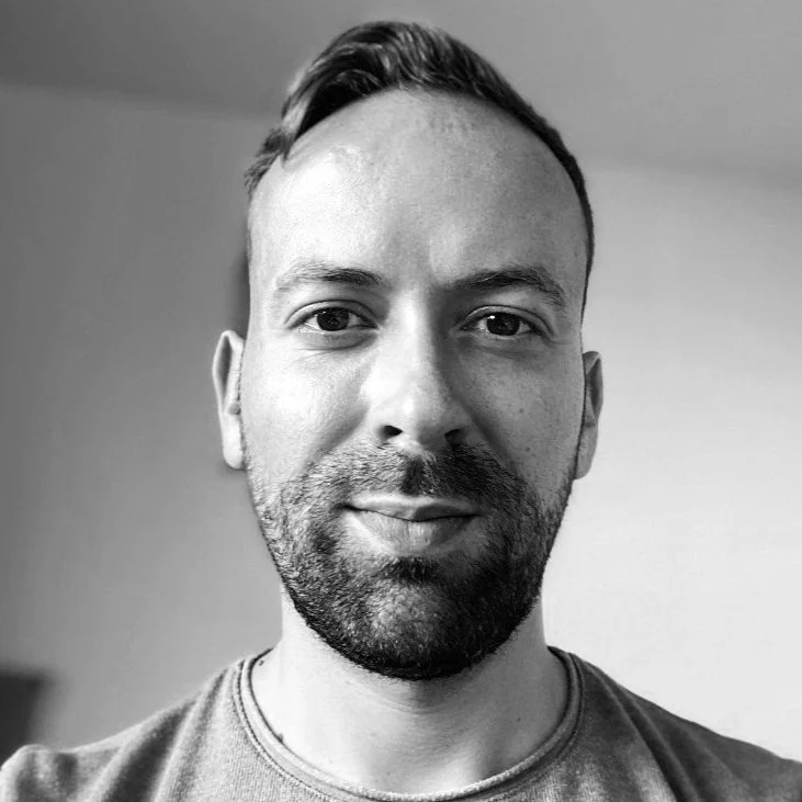 Black and white portrait of a man with short hair and beard, looking at the camera.