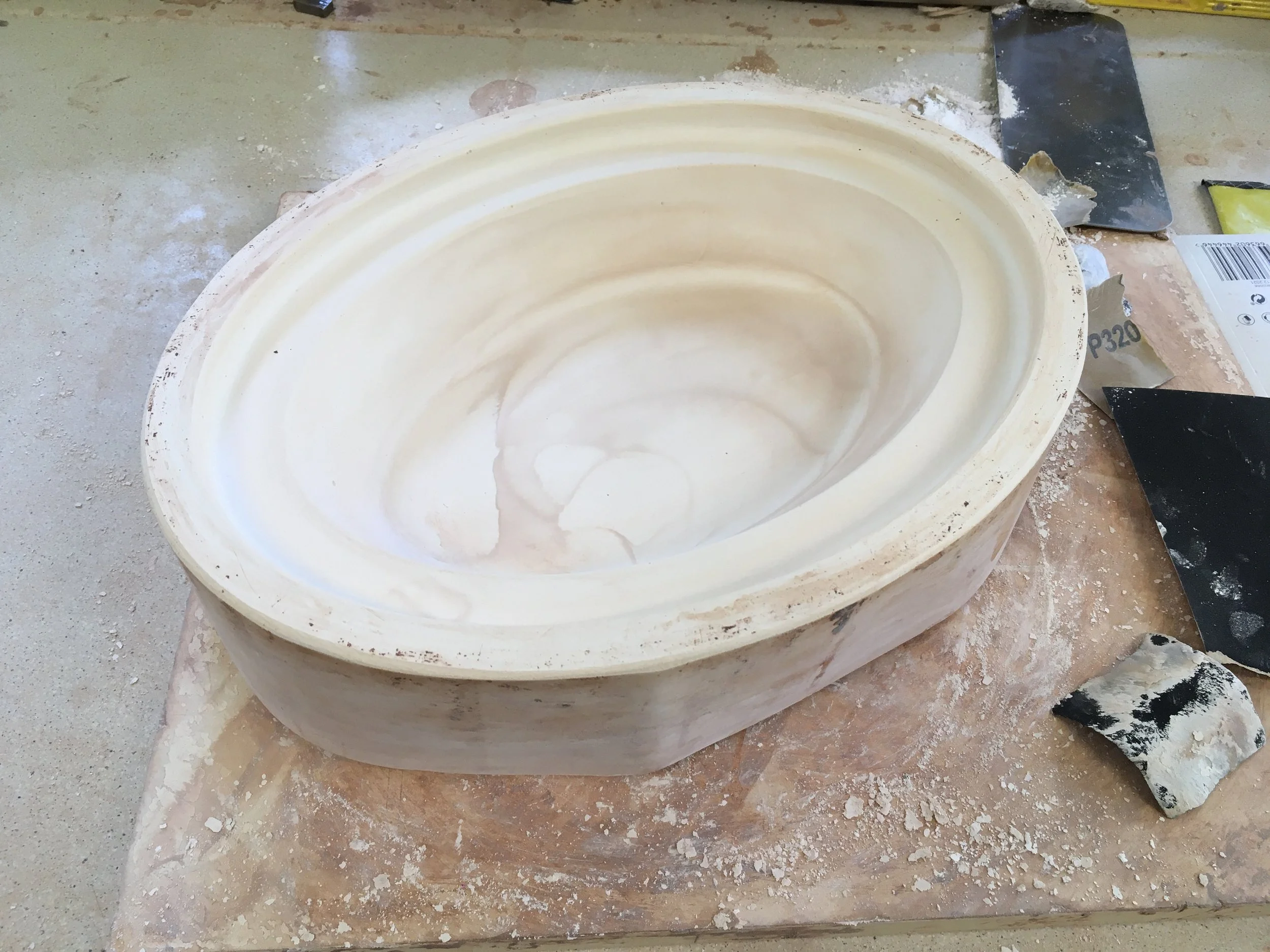 Unfinished ceramic sink mold on a workbench with carving tools and clay debris.